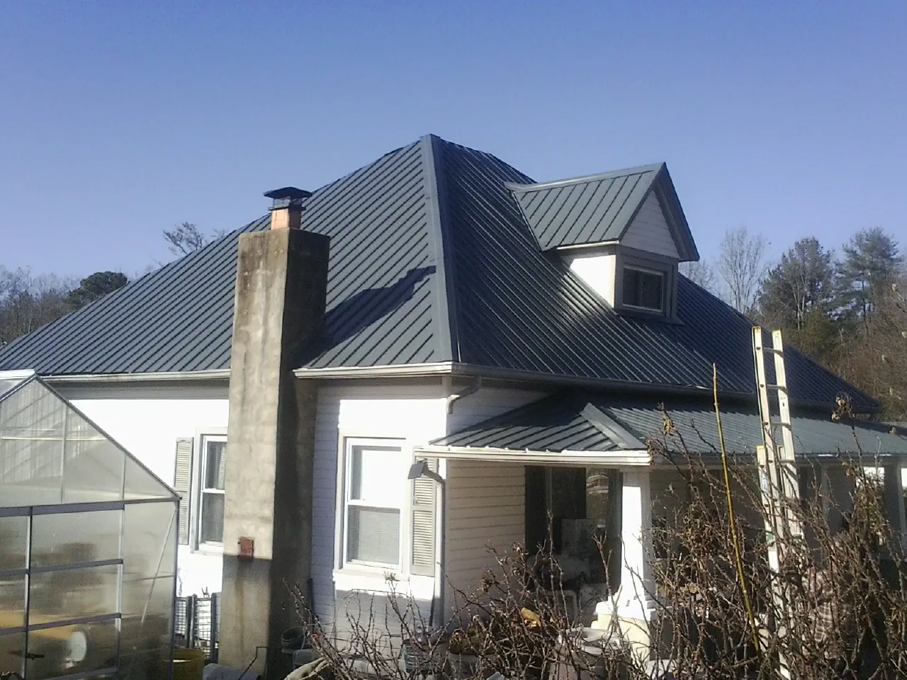 Dark blue standing seam metal roof on a white farmhouse with dormer — Slate & Tile Roof Repair by Roofing Brothers in Binger