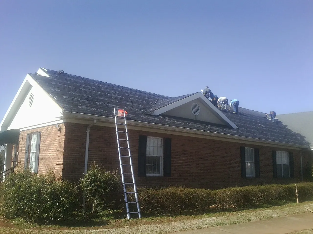 Crew tearing shingles off a brick ranch roof with a ladder set — Metal Roof Repair work by our crew in Binger