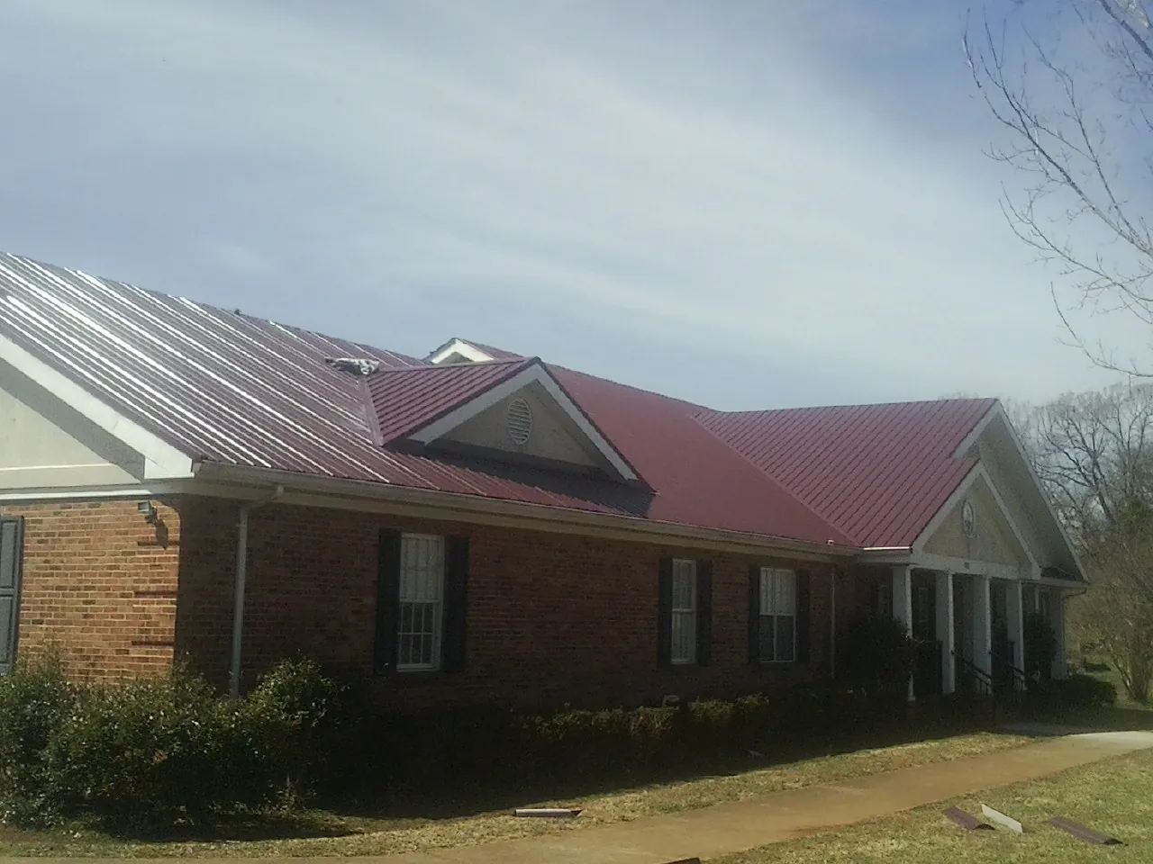 Red metal roof with gabled entries on a long brick building, from a Hail Damage Roof Repair job in Binger