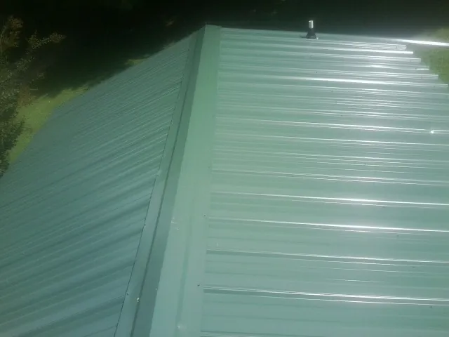 New green metal panels meeting at the ridge of a roof — Flat Roof Repair work by our crew in Binger