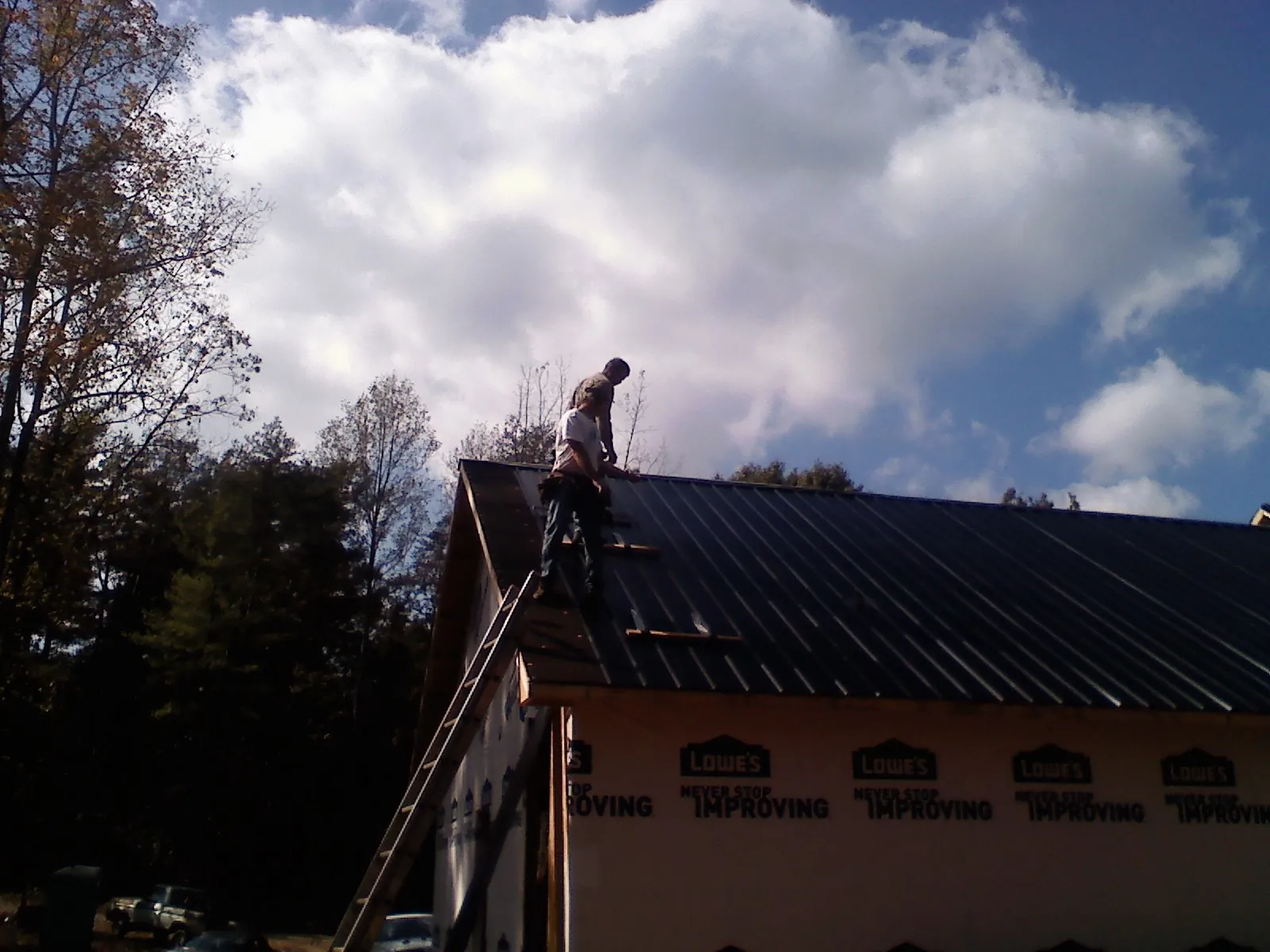 Roofer fastening dark metal panels high against a cloudy sky, from a Roof Inspection job in Binger