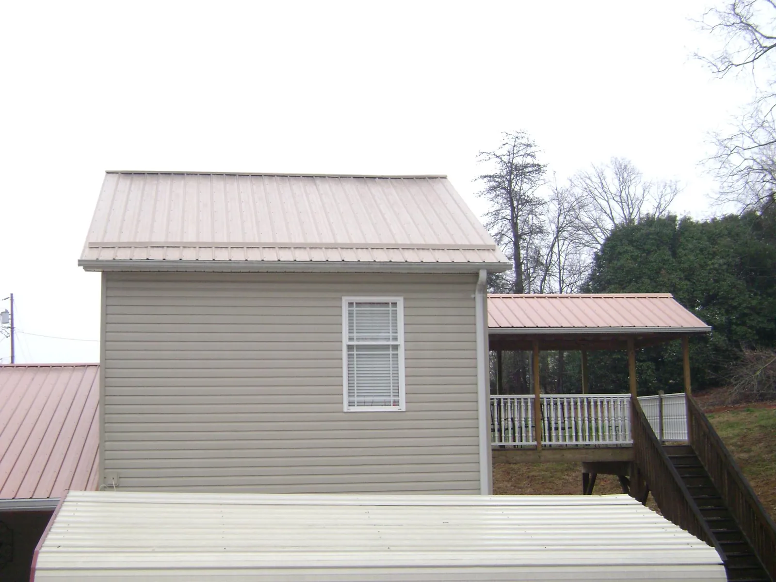 Tan metal roofs on a two story addition and attached porch, from a Roof Replacement job in Binger